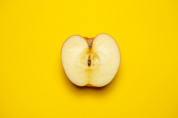 A juicy organic red apple cut in half on a yellow background. Cool minimal flat lay, copy space