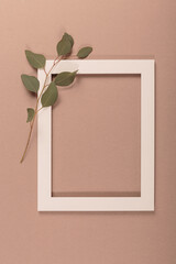 Mockup with beautiful fresh eucalyptus branches and empty frame over pastel beige background. Minimal greeting card or advertising template. Flat lay, top view with copy space for text
