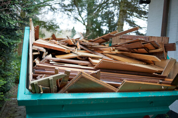 green recycling container filled with wood, next to a house