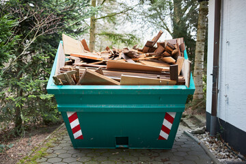 green container filled with wood, next to a house