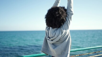 African american woman wearing sportswear stretching arms at seaside - Powered by Adobe