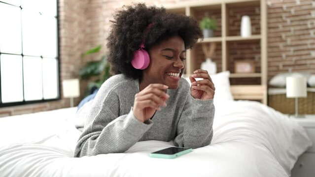 African american woman dancing and listening to music lying on bed at bedroom