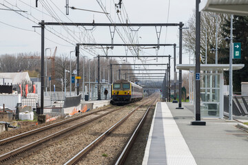 View of a belgian train standing on the platform in Diepenbeek, and public work performed at the side of the rail track.
