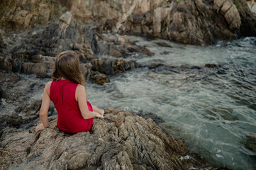 blond girl in a red dress sitting on the rocks