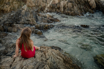 girl in a red dress sitting on the rocks near the sea