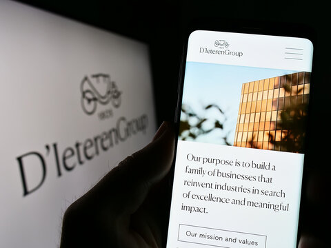 Stuttgart, Germany - 03-18-2023: Person holding smartphone with webpage of Belgian automotive company D'Ieteren S.A. on screen in front of logo. Focus on center of phone display.