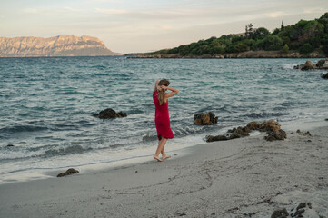 woman in a red dress walking barefoot on a beach  