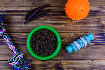 Bowl with pet food, dog toy for teeth cleaning, rope with tied knots and toy ball on a wooden background. Top view