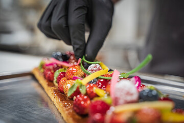 Hand of a chef placing ingredients in a fruit tart.