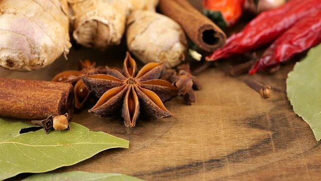 Falling dried clove buds on a wooden board against the background of ginger root, red chili pepper, star anise, bay leaf and garlic.