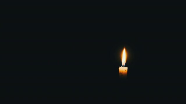 One candle is lit on a black background. Close-up of a yellow flickering flame illuminates the darkness. Isolated, Copyscape. The warm glow of flame burning at night and moving with the wind. 4K