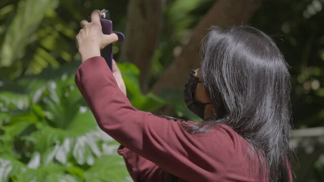 This video shows an old senior woman wearing a mask and taking nature photos with her phone.