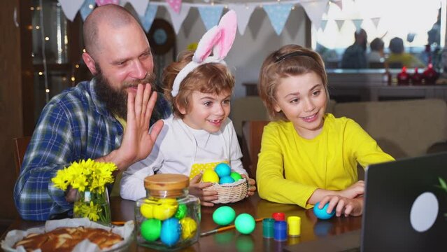 Happy family Easter tradition. Remote greeting relatives using laptop, painting egg, bunny ears. Christian religious holiday Sunday togetherness
