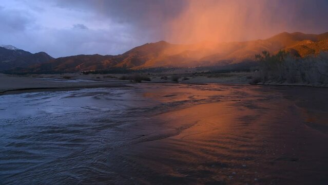 Sunset Medano Creek - A ray of twilight illuminates misty clouds hovering over rolling hills and rushing Medano Creek on a stormy Spring evening. Great Sand Dunes National Park & Preserve, CO, USA.
