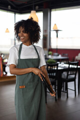Portrait of young African waitress smiling holding a tray with restaurant background.