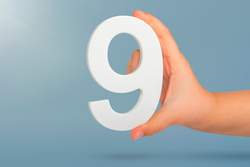 Number nine in hand. A hand holds a white number 9 on a blue background. Concept with number nine....