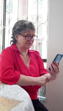 older woman checking her cell phone next to a large window