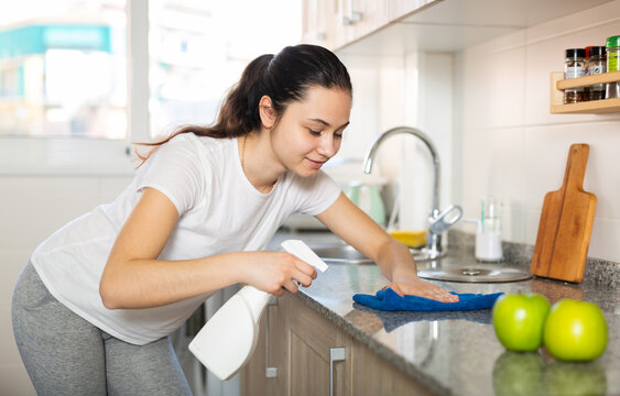 Young woman cleaning kitchen surfaces using sponge and spray cleaner