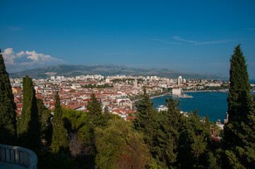 Fototapeta na wymiar A balcony overlooking a forest, the city of split and a bay with ships in the harbor