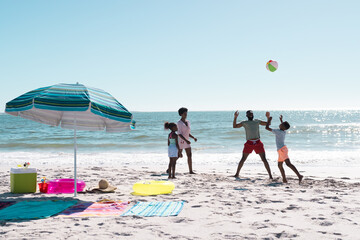 African american parents and children playing with ball while enjoying at beach against sea and sky
