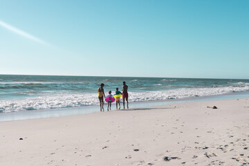 Rear view of african american parents and children with swimming float running towards sea under sky