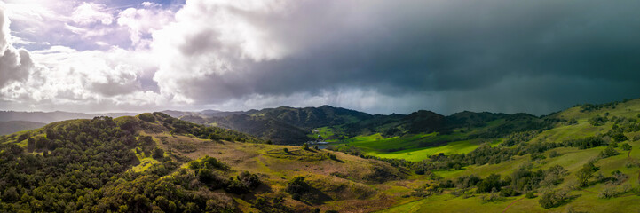 Obraz na płótnie Canvas Panoramic view of bright sun and dark storm clouds over green California landscape