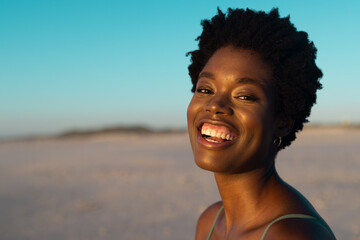 African american mid adult woman with afro hair laughing at beach under clear sky at sunset