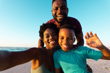 Portrait of african american woman taking selfie with happy husband and son at beach against sky
