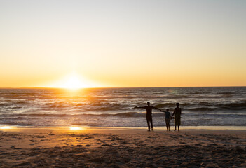 Fototapeta na wymiar Silhouette african american son holding mother and father's hands and standing on beach at sunset