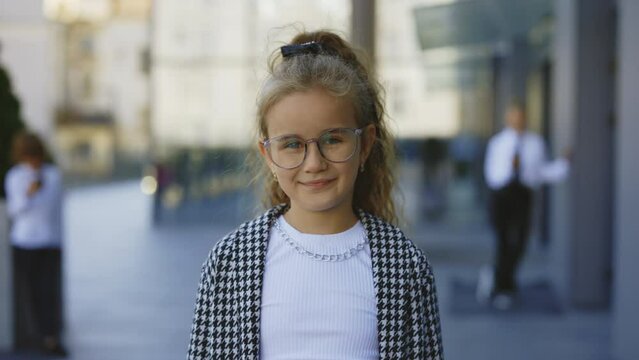 Portrait of the beautiful little businesswoman wearingg glasses in formal suite standing near office centre. Girl manager looking at camera. Kids portrait