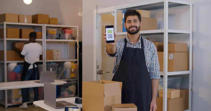 Portrait of warehouse worker man smiling and showing at camera smartphone with vaccination qr-code - Powered by Adobe
