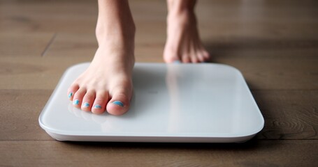 Young girl teenager steps on white scales to measure control weight. Teen checks body mass and fat, healthy dieting and fitness concept. - obrazy, fototapety, plakaty