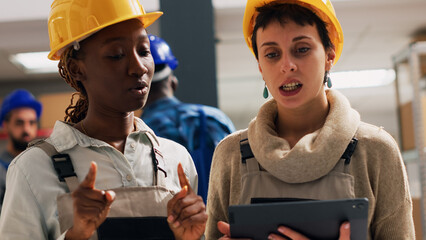 Depot managers in overalls using tablet for inventory, planning distribution and logistics for delivery service. Team of diverse people checking stock products in storage room. Handheld shot.