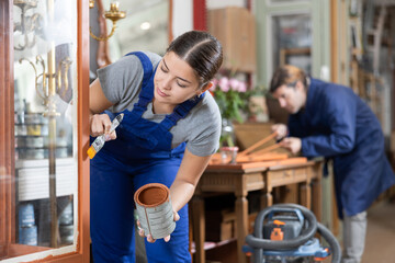 Young female furniture workshop worker repainting vintage glass cabinet