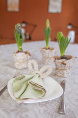 Spring festive dining table setting with flowers, napkins and cute bunny decor on linen tablecloth. Easter time. Cozy home
