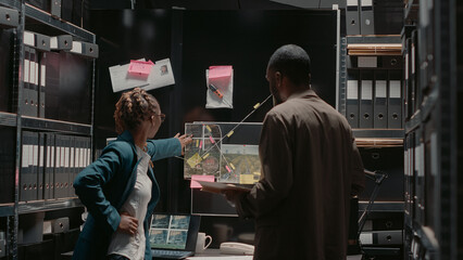 Inspectors studying crime case files in evidence room to find suspect, team of police agents...