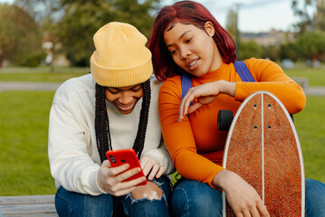 two hispanic teenage girls using a smartphone in a relaxed time with friends. friends having a good...