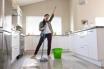 Cheerful caucasian young woman with hand raised dancing, singing and cleaning floor with wet mop