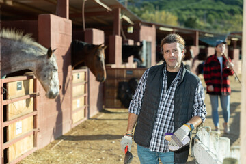 Man in front of his farm and stables with horses