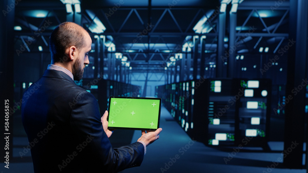 Poster system engineer checking green screen display on tablet, running mainframe diagnostics in data cente