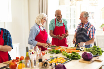 Happy group of diverse senior friends in aprons talking during cookery class