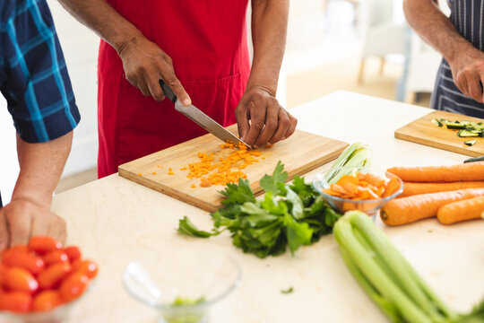 Hands of diverse senior friends wearing aprons cutting vegetables during a cookery class