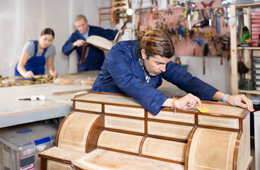 Craftsman inspects and prepares vintage chest of drawers for restoration in a restoration workshop