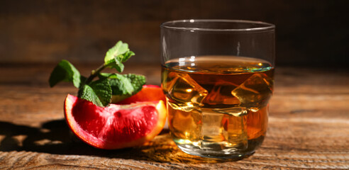 Glass of rum with ice, mint and Sicilian orange on wooden table, closeup