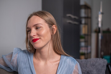Naklejka premium The young beautiful smiling woman with beautiful long hair, red lips and light blue dress. A wardrobe and a bookshelf in background.