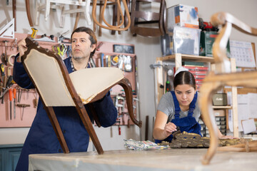Professional male and female artisans restorers in uniform renovating antique chair mirror frame...