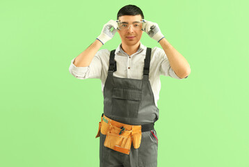 Young carpenter in safety goggles on green background