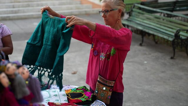 Pretty mature senior, woman tourist wearing ethnic clothes shopping for handicrafts from a street vendor in Merida, Mexico.