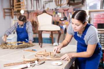 Young female furniture workshop worker carving wooden vintage chair parts