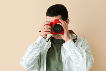 Young male photographer with professional camera on beige background, closeup